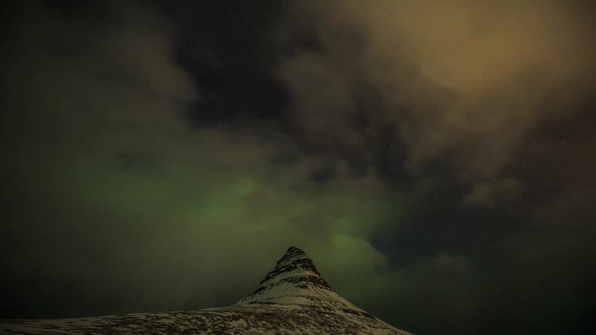 Clouds and northern lights above a snowy mountain peak