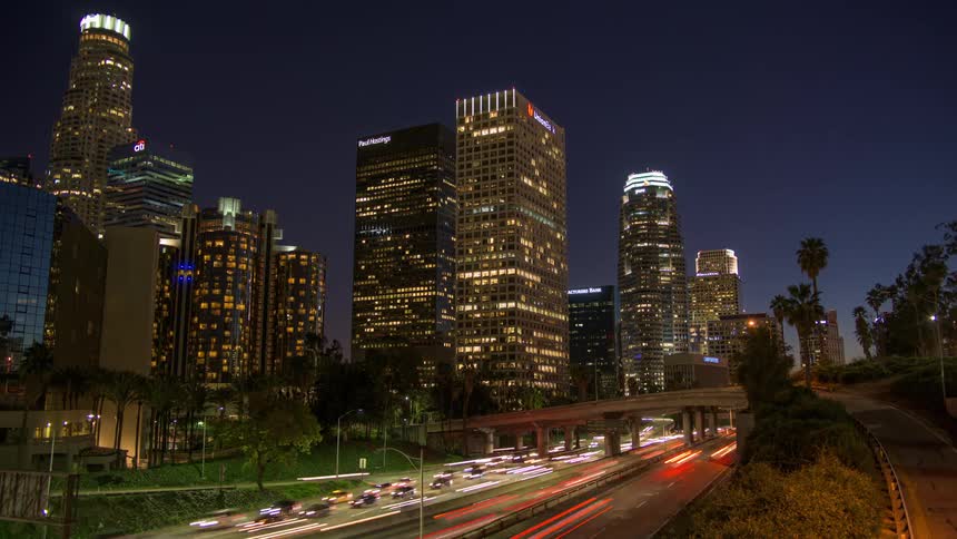 Dense traffic drives down a highway past downtown at night