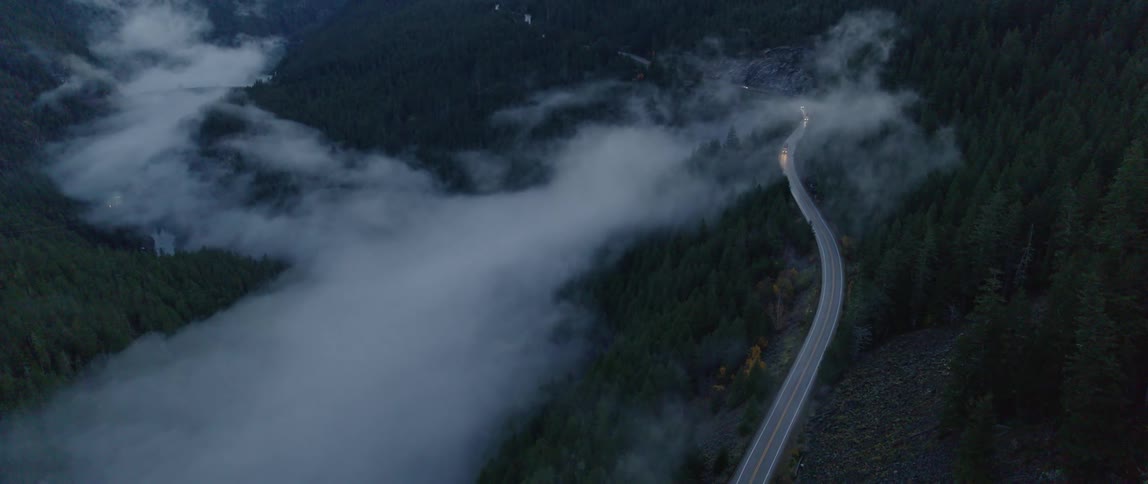 Cars traveling on a curving mountain road through low clouds