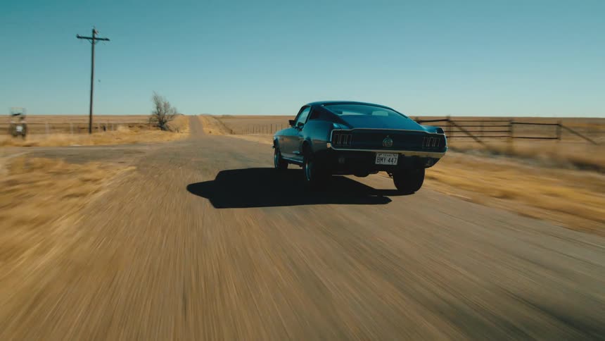 Black car travels fast on a rural road under a blue sky