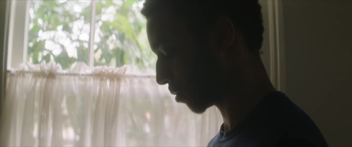 A man in a blue shirt looks down near a window