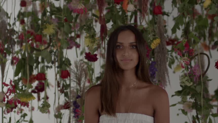 A woman standing in front of vines with flowers smiles