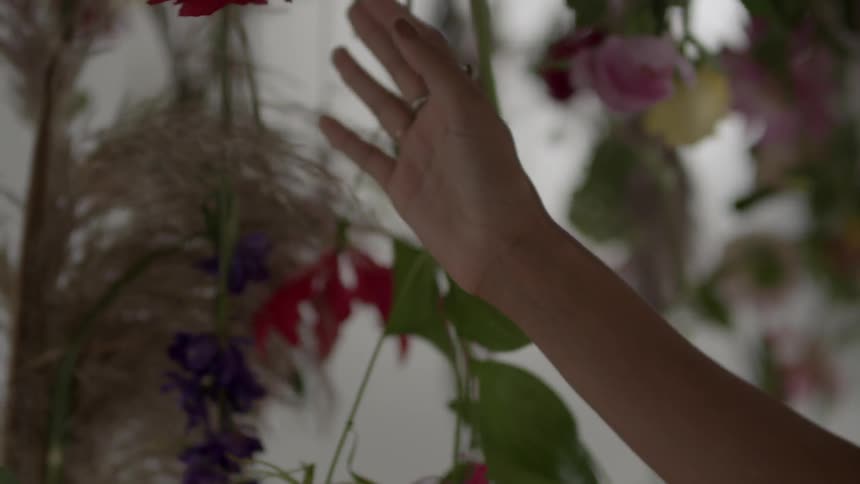 A hand brushes against vines with flowers hanging
