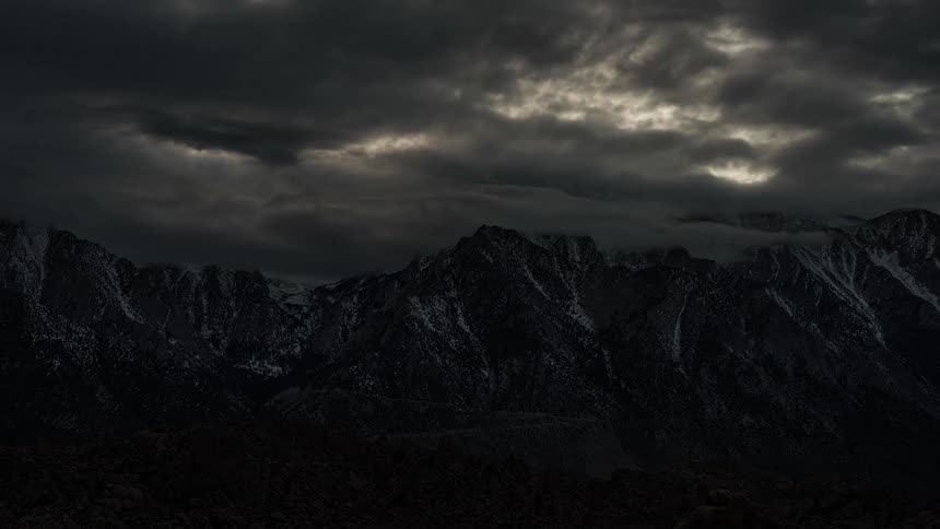 Dark clouds accumulate over the snowy mountains as night approaches