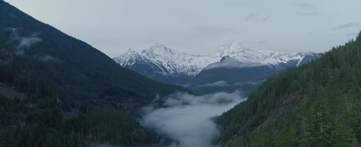Fog sits in a valley by snow capped mountains