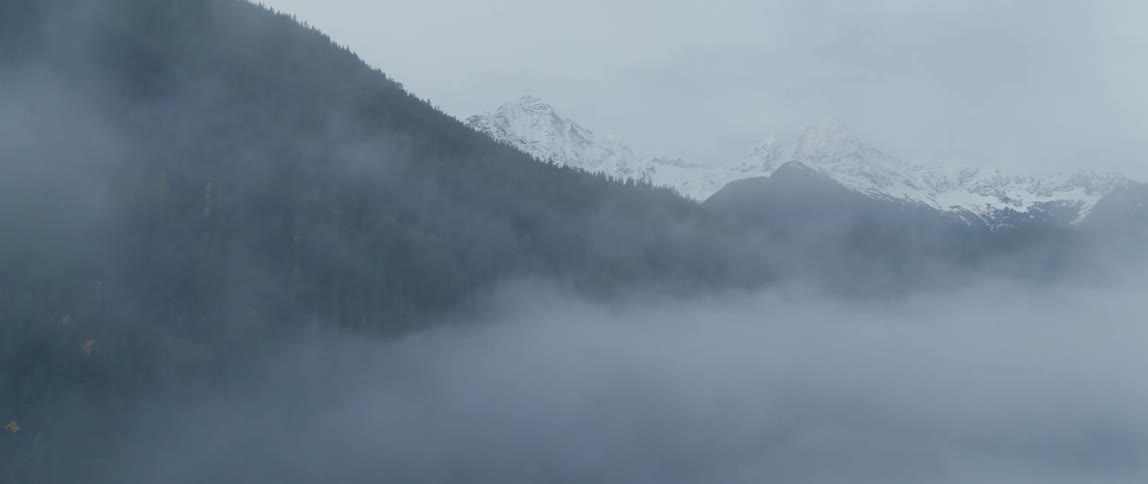 Aerial through clouds to snow covered mountains