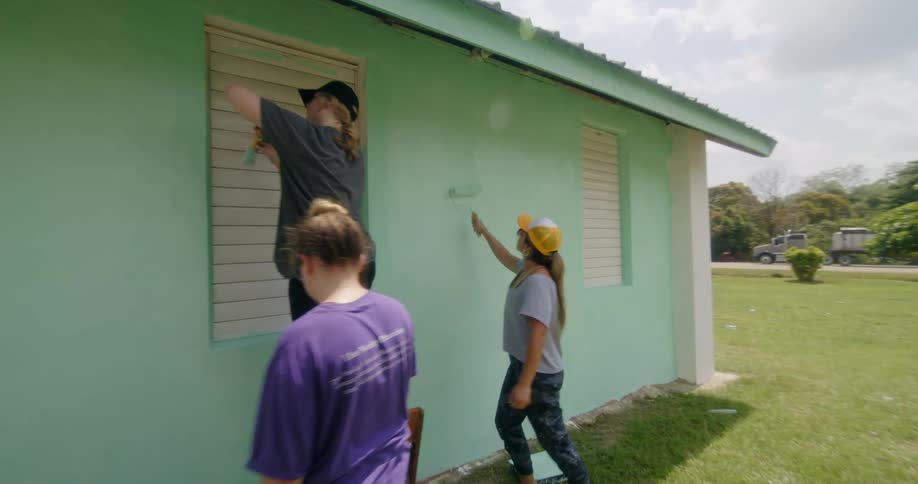 A group of women work together painting a house
