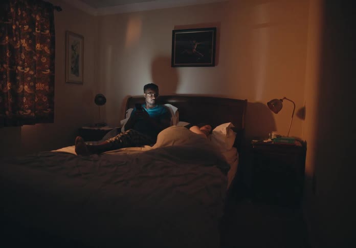 A man is dressed and sitting up in bed and his wife is sleeping next to him