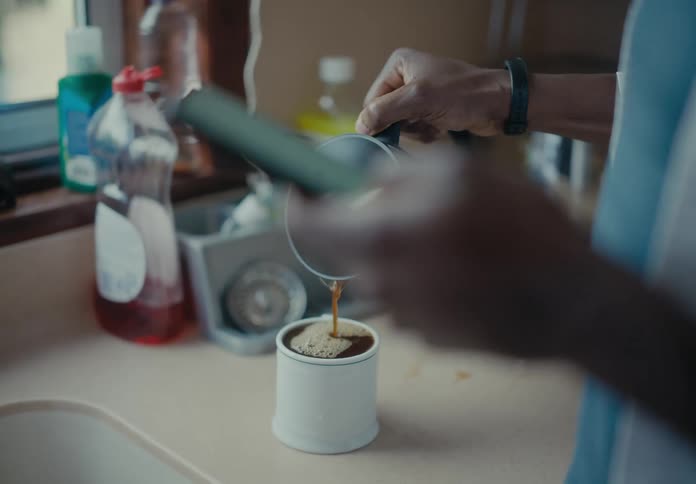A man pouring and spilling coffee while being distracted by scrolling on a smartphone