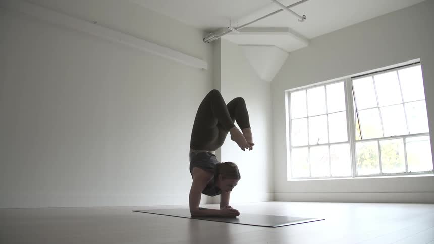 A woman performs a difficult yoga pose in an open, airy room during the day