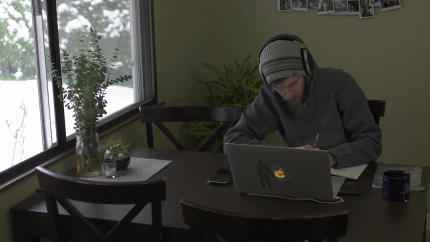 A man is writing at a table by the window