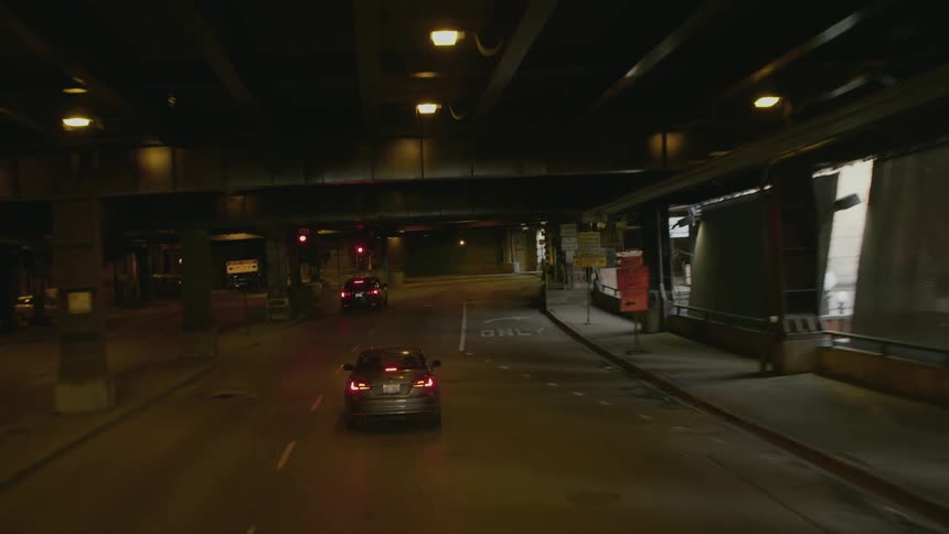 A car in a city drives through an underpass and comes to a stop at a traffic light