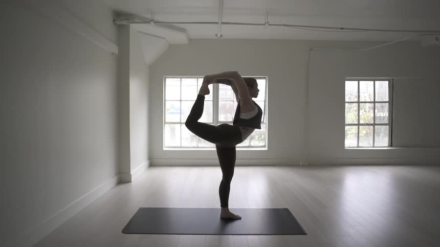 Woman performs standing bow yoga pose in yoga studio