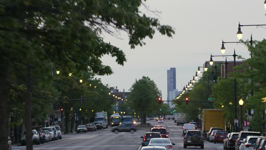 Automobiles are traveling on a downtown street as birds fly overhead and there is a skyscraper at the end of the road