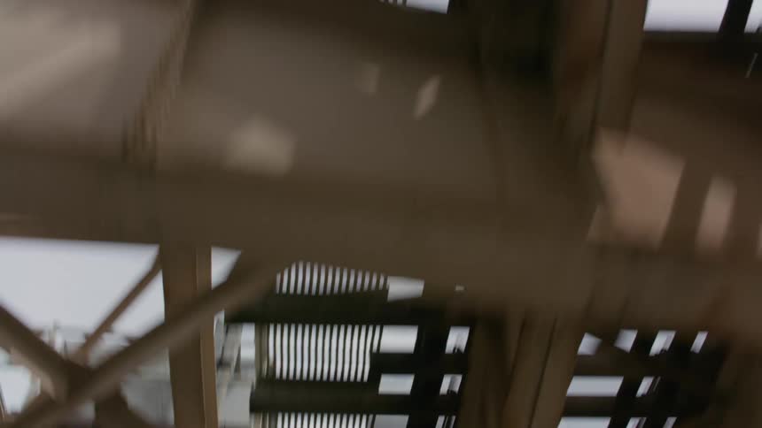 Moving footage of the underside of a bridge with train tracks against blue sky