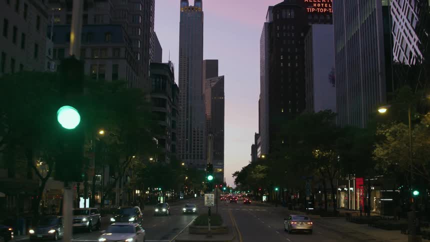 Traffic moves on a busy downtown street lined with lined with large building lit up at night