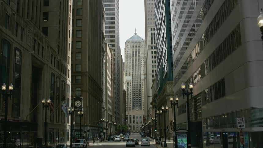 Cars and pedestrians on a chicago city street with the chicago board of trade building at the end