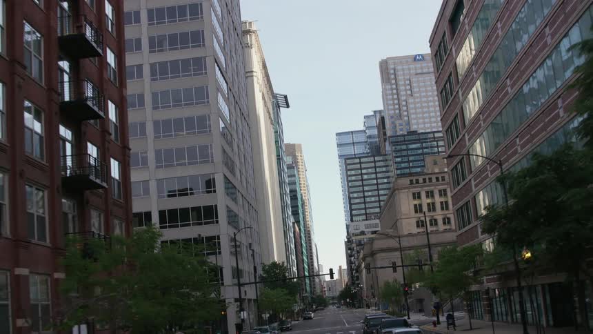 Light traffic is on a downtown street surrounded by tall buildings and skyscrapers and moving through an underpass