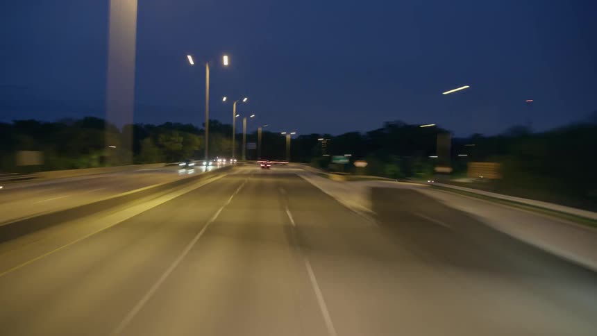 Vehicles move along controlled access highway and under bridge at night