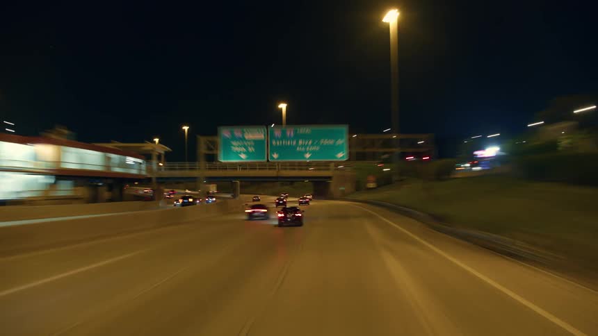 Time lapse of cars driving past businesses on a freeway at night