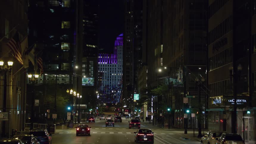 A silhouetted display illuminates the side of a building on a busy chicago city street at night