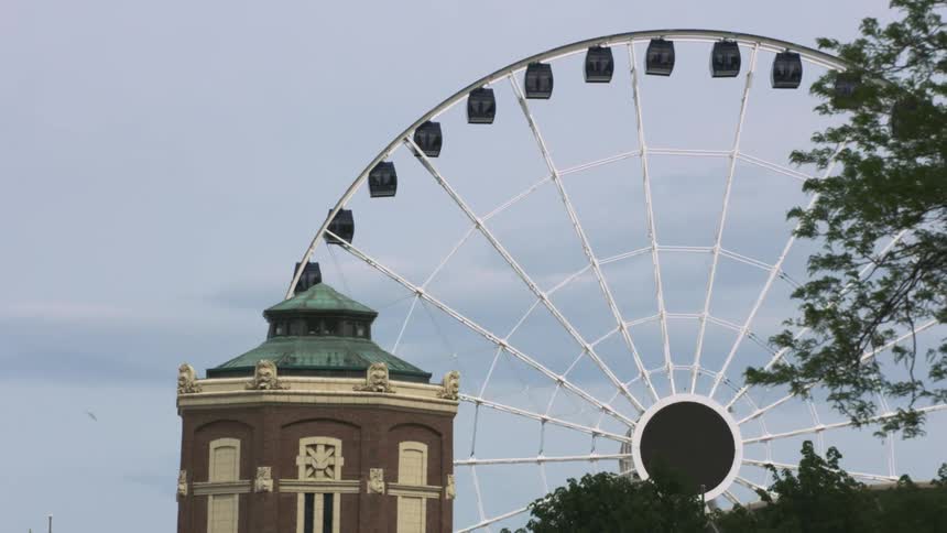 A ferris wheel turns near a tower and buildings
