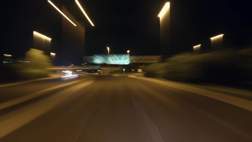 Vehicles drive very fast past apartment buildings and condos in a city at night
