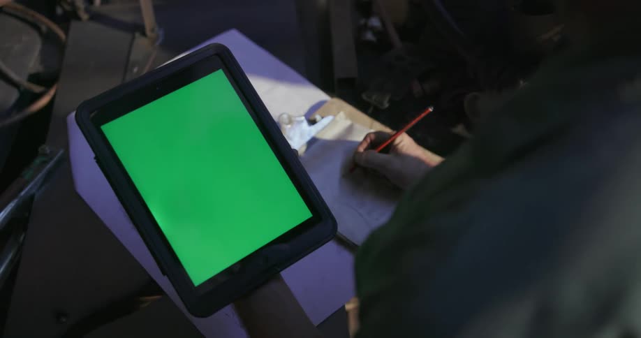 A man uses a tablet as he writes in his pad
