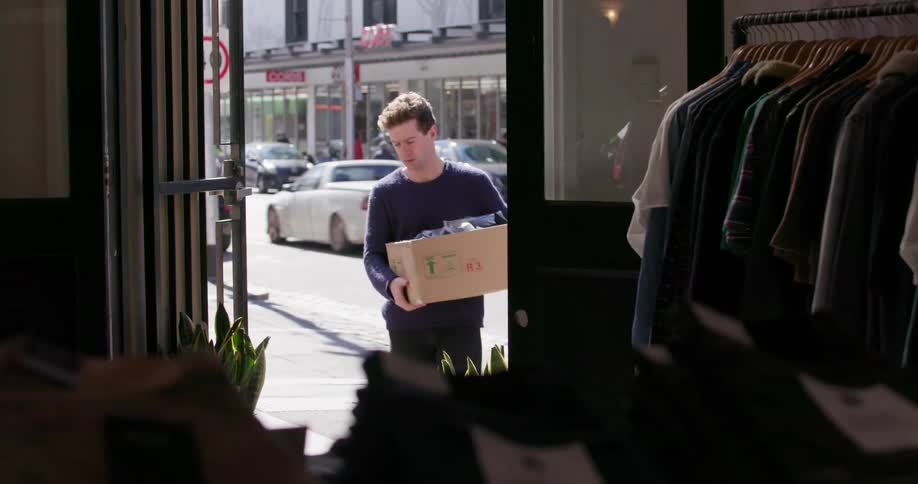 Man carrying box walks into a clothing shop