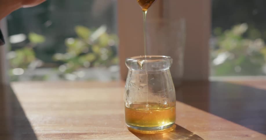 A hand stirs honey in a jar