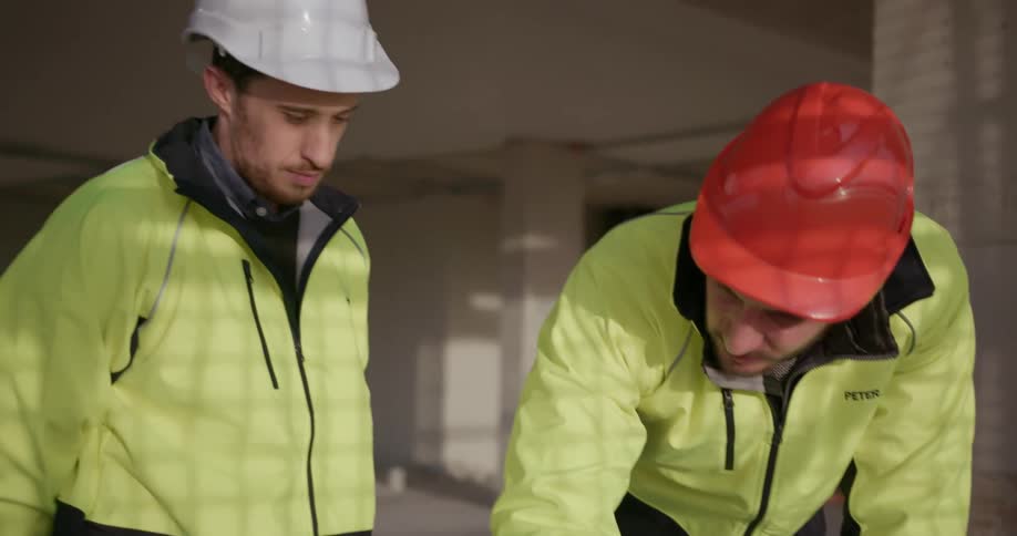 Two workers look over some blueprints in a building