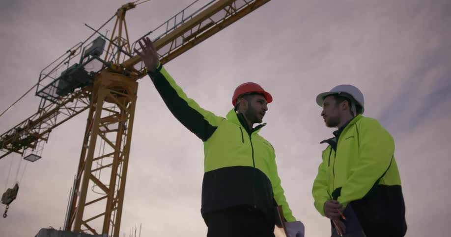 Two construction workers talk beneath a crane
