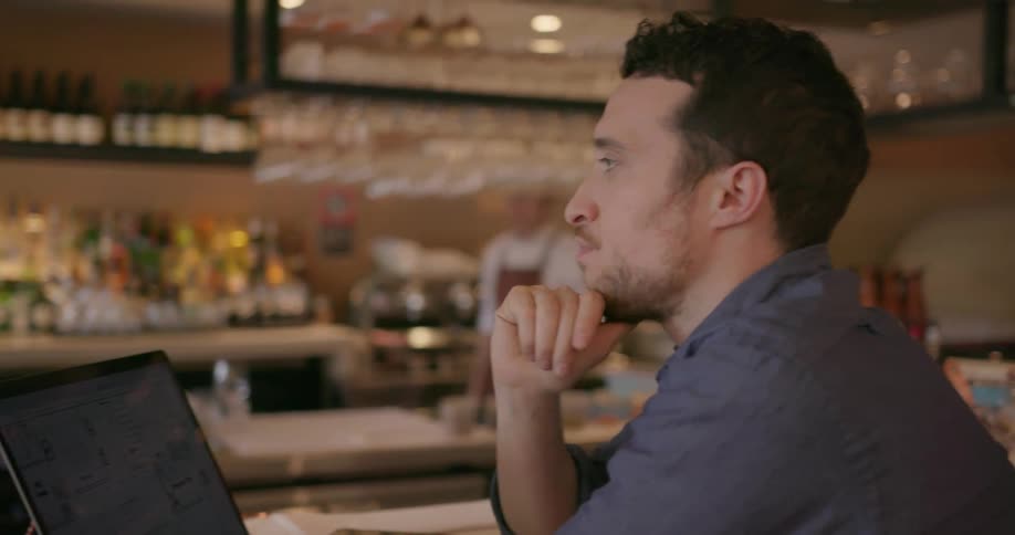 Man sits at a bar looking at his laptop