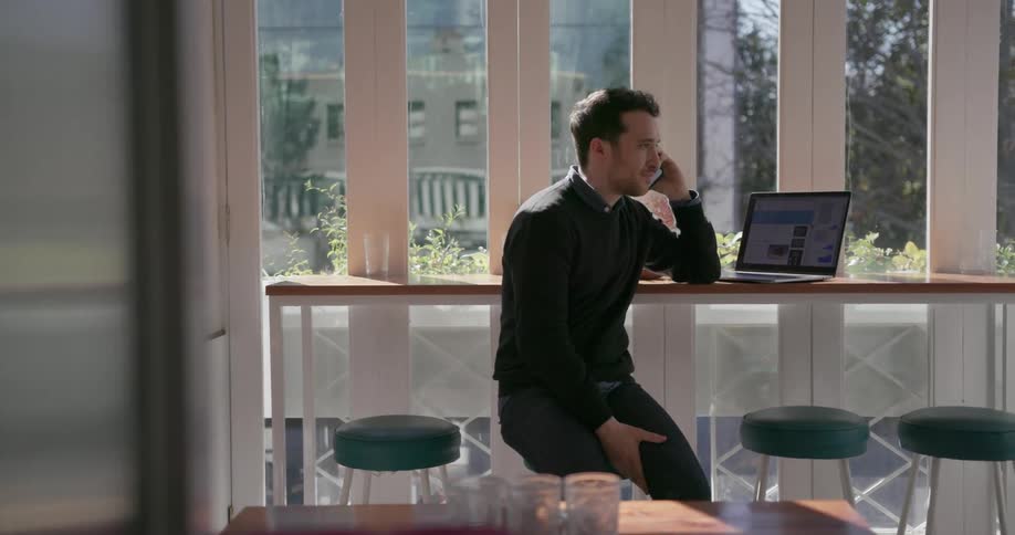 A man sits on a stool in a restaurant talking on his cell phone