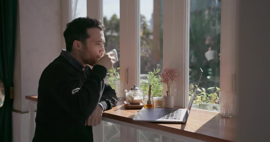 A man looks out the window in a cafe and takes a drink