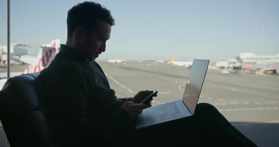 Man sits in airport lounge working on his laptop