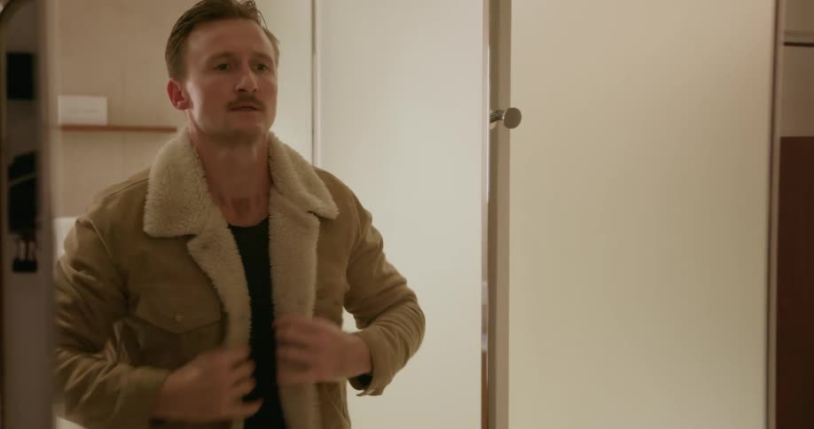 Man puts on coat while looking in mirror