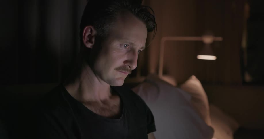A man is using a laptop as he sits in bed at night