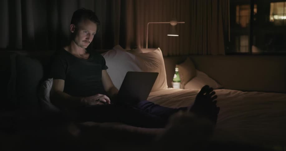 A man sits in bed using a laptop