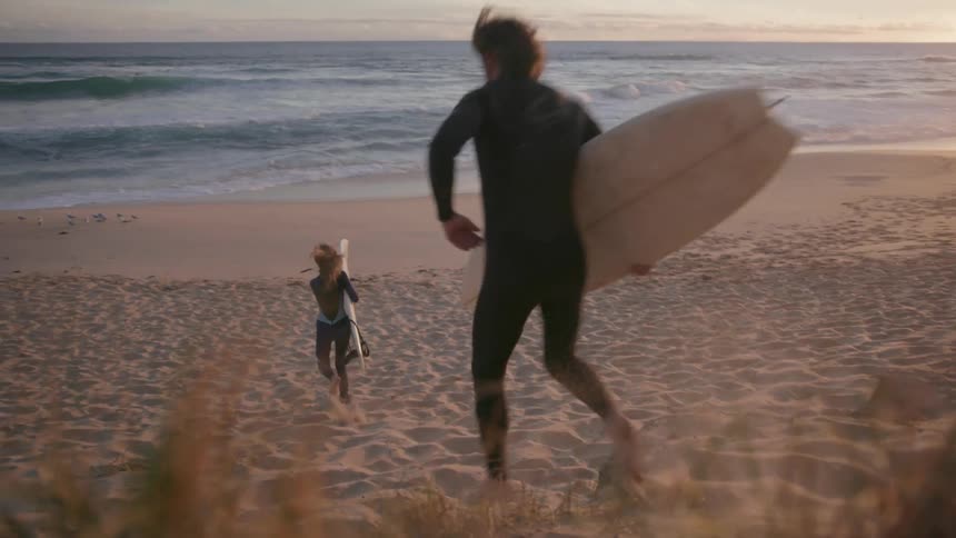 Surfers run towards the ocean at sunset