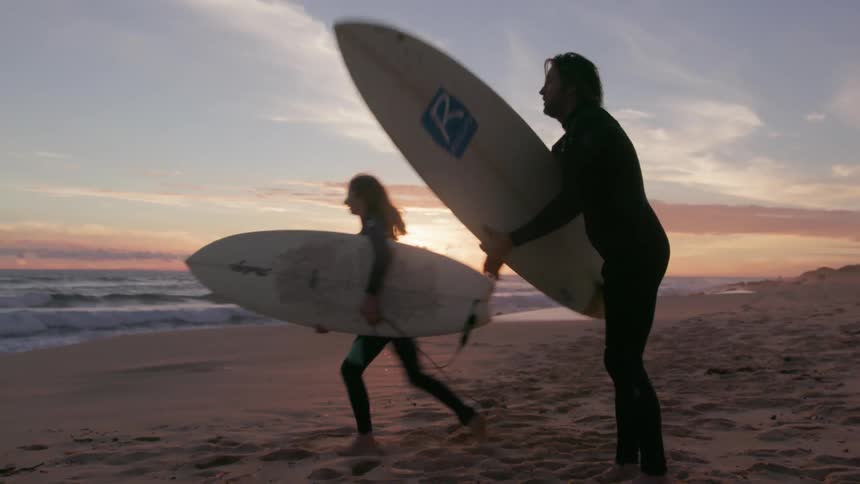 Surfers run towards the ocean at sunset