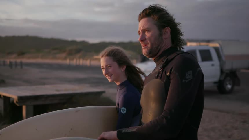 Man and girl talk while each holds a surfboard