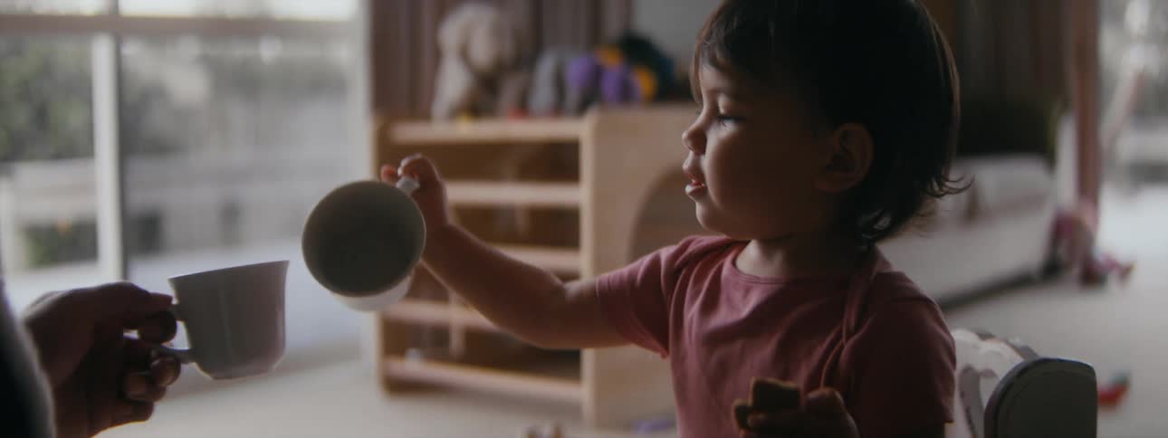 A toddler is playing with a cup while sitting indoors