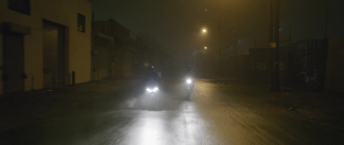 Two people ride motorcycles at night