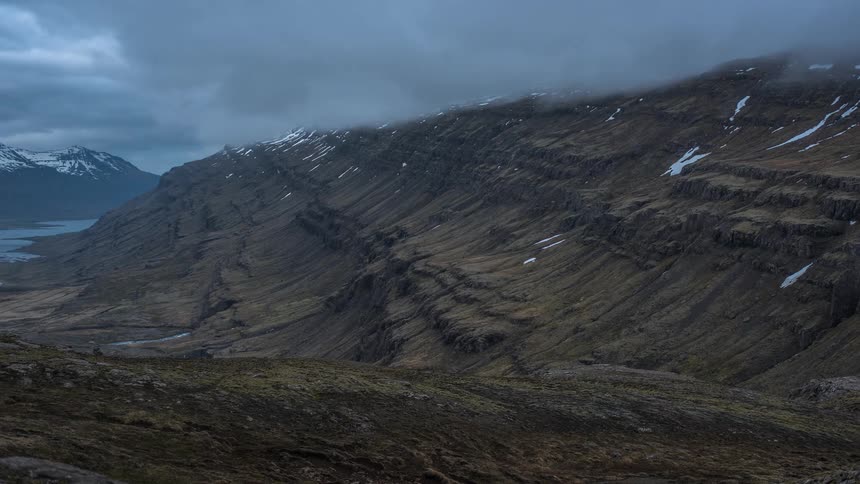 Heavy clouds settle over a snow capped canyon and lake