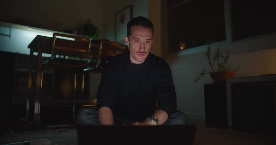 A man uses his laptop while sitting on the floor of his living room