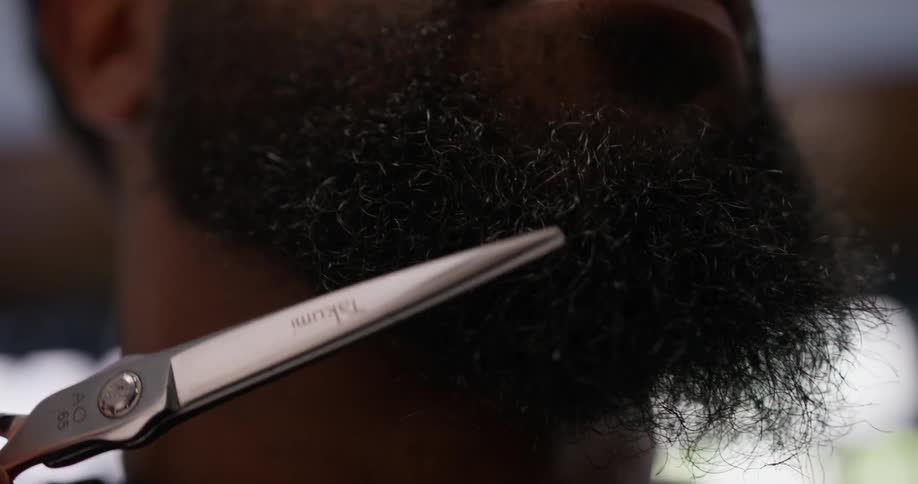A mans beard is being trimmed with scissors