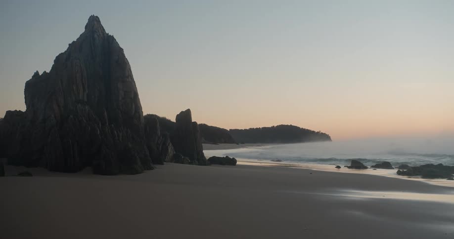 Large formations of rock on a sandy beach during the day