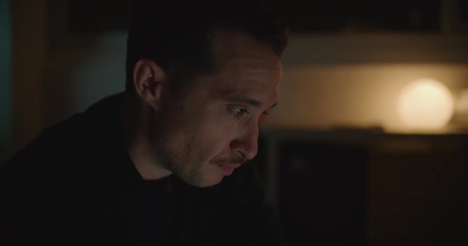 A man looks worried as he sits in a dimly lit room