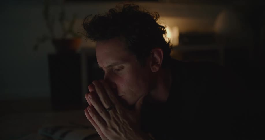 A man lying down on his living room floor typing on his laptop pauses to think
